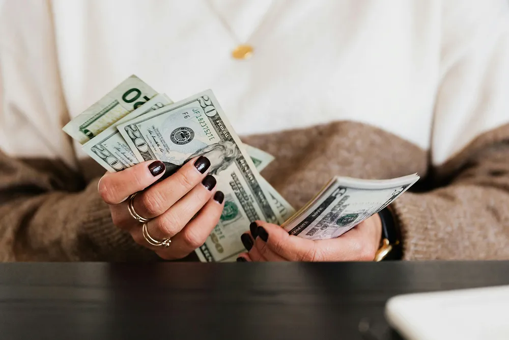 A person holding a stack of U.S. dollar bills, representing savings that can be allocated to FSA or HSA accounts for healthcare expenses.